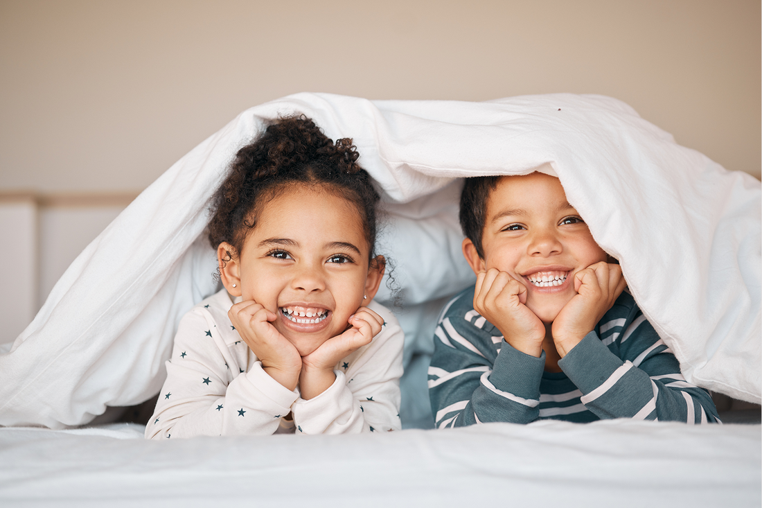 two siblings smiling with their heads peaking out from under a blanket