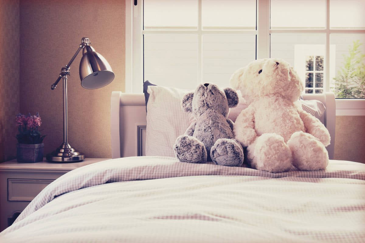 Vintage photo of kids room with dolls and pillows on bed and bed