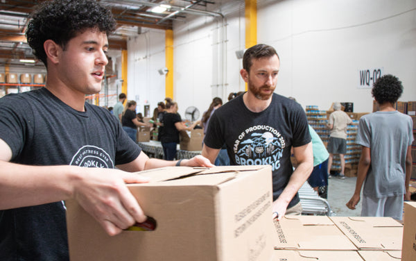 Two men in a warehouse setting, one handing a box to the other.