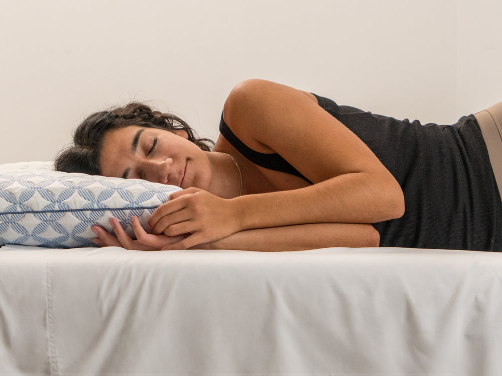 Woman sleeping on a bed with a Luxury cooling pillow, wearing a black tank top.