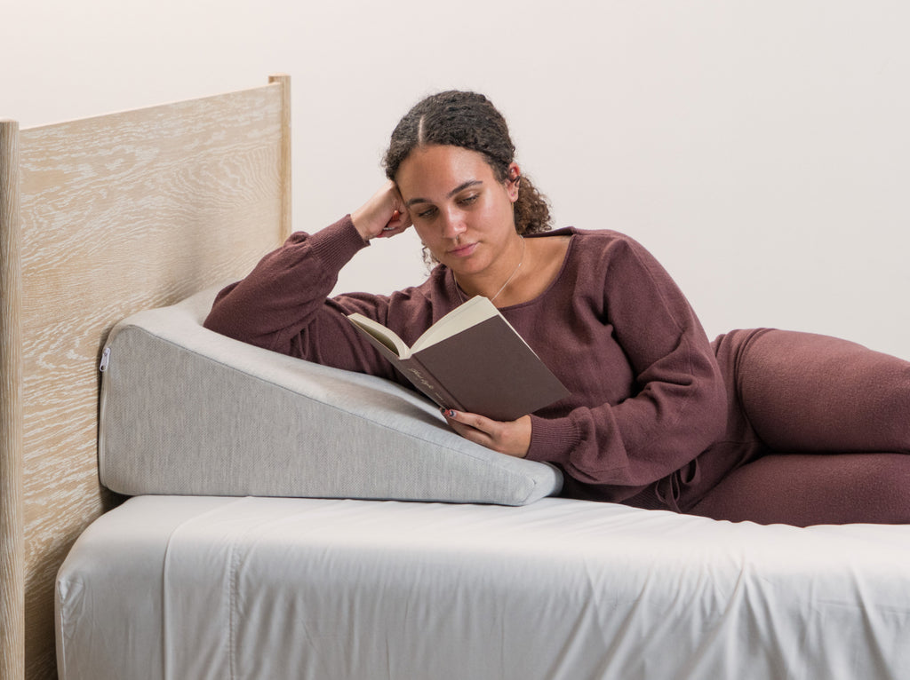 Woman reading a book on a wedge-shaped pillow in bed