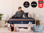 Two adults pose around the Brooklyn Bedding Aurora Luxe Cooling mattress in a bright bedroom, with award badges above and a “New And Improved Design” text box in the lower right.