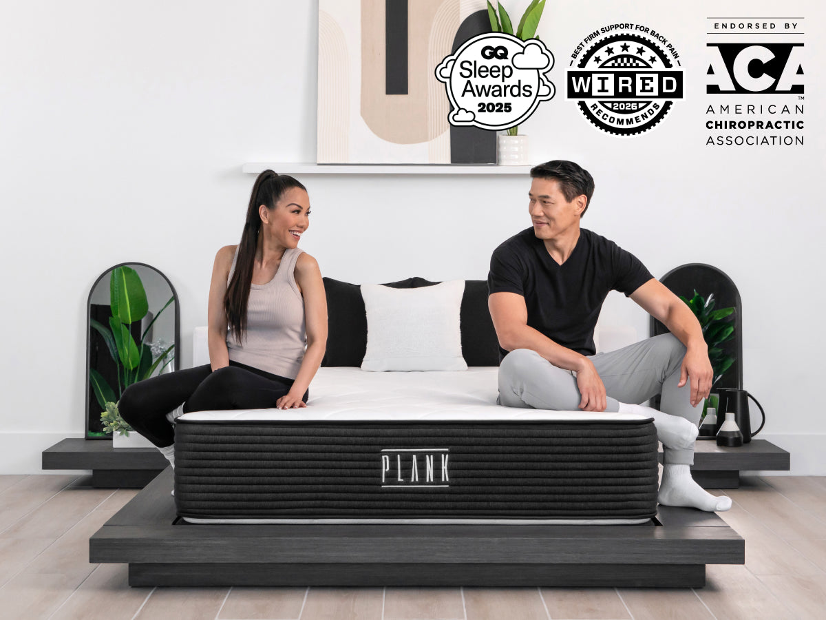 Brooklyn Bedding Plank Firm Luxe mattress with two people sitting on the bed, with badges reading “GQ Sleep Awards 2025,” “WIRED Recommends 2025,” and “Endorsed by ACA American Chiropractic Association.”