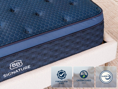 Close-up of the Brooklyn Bedding Signature Hybrid showing the blue quilted top, side panel, and badges reading “Fiberglass Free,” “GREENGUARD Gold,” and “CertiPUR-US.”
