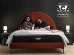 Brooklyn Bedding Titan Plus Core mattress on a rust-colored upholstered bed frame in a stylized bedroom setting with two people relaxing on top. Badge reads: "Endorsed by ACA — American Chiropractic Association."