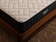 Close-up corner view of the Brooklyn Bedding Titan Plus Core mattress resting on a walnut wood bed frame, showing the cream-colored quilted top panel and charcoal ribbed border.