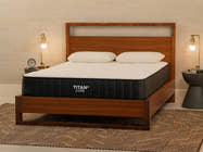  Brooklyn Bedding Titan Plus Core mattress on a walnut wood platform bed in a warm, mid-century modern bedroom with two white pillows, brass sconce lamps, and a woven area rug.