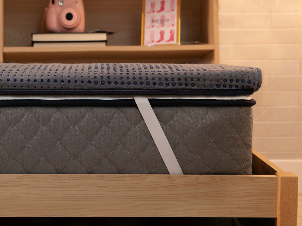 Angled view of the CopperFlex 201 Mattress Topper secured with elastic straps on a wooden bed frame.