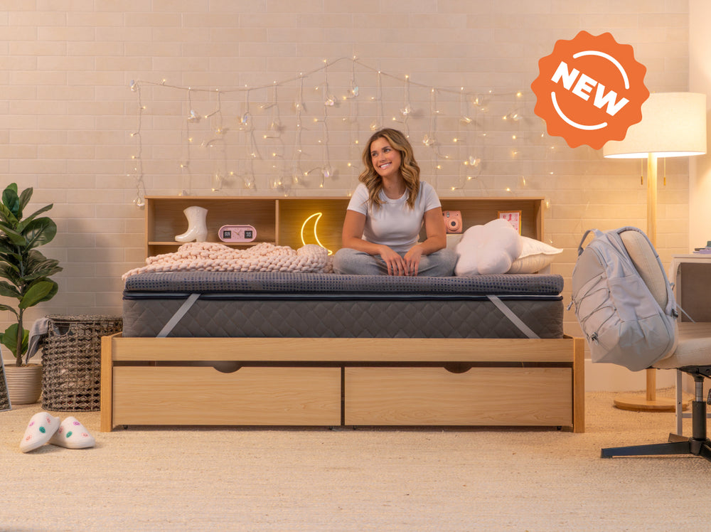 Woman sitting on a bed, with Mattress Topper CopperFlex 2 inch. wooden frame and storage drawers in a cozy bedroom setting.