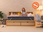 Person sitting cross-legged on the CopperFlex 201 Mattress Topper on a bed with headboard shelving and string lights.