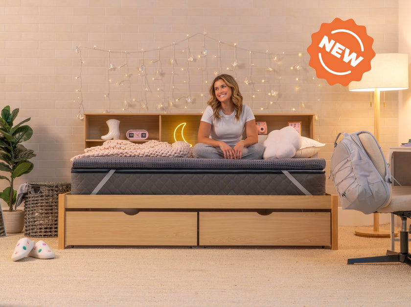 Person sitting cross-legged on the CopperFlex 201 Mattress Topper on a bed with headboard shelving and string lights.