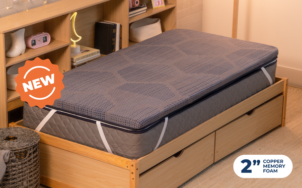 Woman sitting on a bed, with Mattress Topper CopperFlex 2 inch. wooden frame and storage drawers in a cozy bedroom setting.