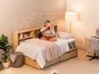 Person sitting cross-legged on the CopperFlex 301 Mattress Topper on a bed with headboard shelving and string lights