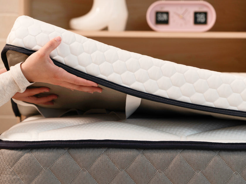 Hands lifting the CopperFlex 301 Mattress Topper to show flexibility, quilted cover, and elastic corner strap.