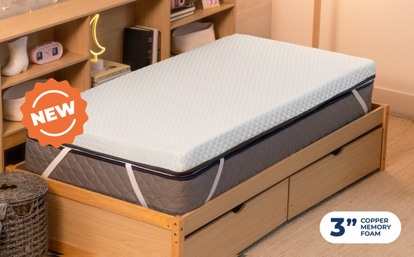 Person lying on the CopperFlex 301 Mattress Topper wearing headphones on a bed with storage frame.

