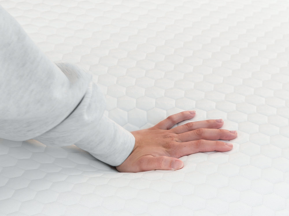 Hand pressing into the surface of a white hexagon-quilted mattress topper to show cushioning and responsiveness.