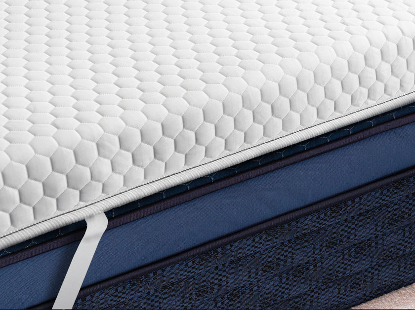 Angled close-up of a white mattress topper with hexagon-pattern quilted cover and piped edge detailing.