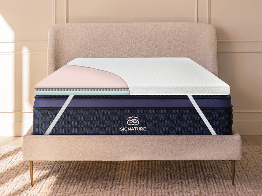 Cutaway view of mattress topper on a bed revealing internal foam and microcoil layers beneath the quilted cover.