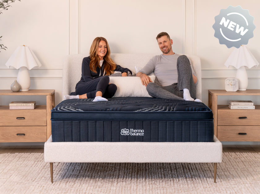 Couple sitting on a bed with a mattress labeled  Brooklyn Bedding Thermobalance in a bedroom setting.