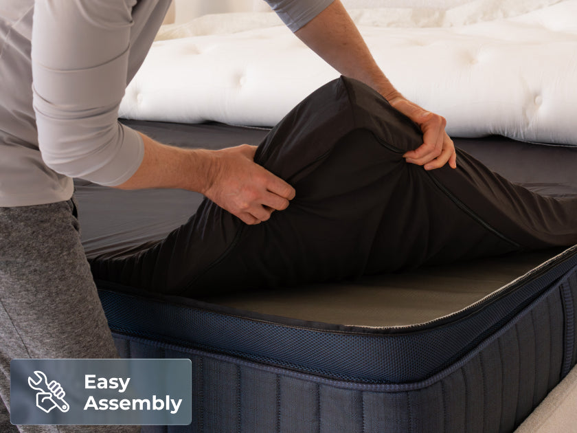 Man unrolling a compressed, dark blue mattress onto a bed frame. Text overlay: "Easy Assembly" with a wrench icon.