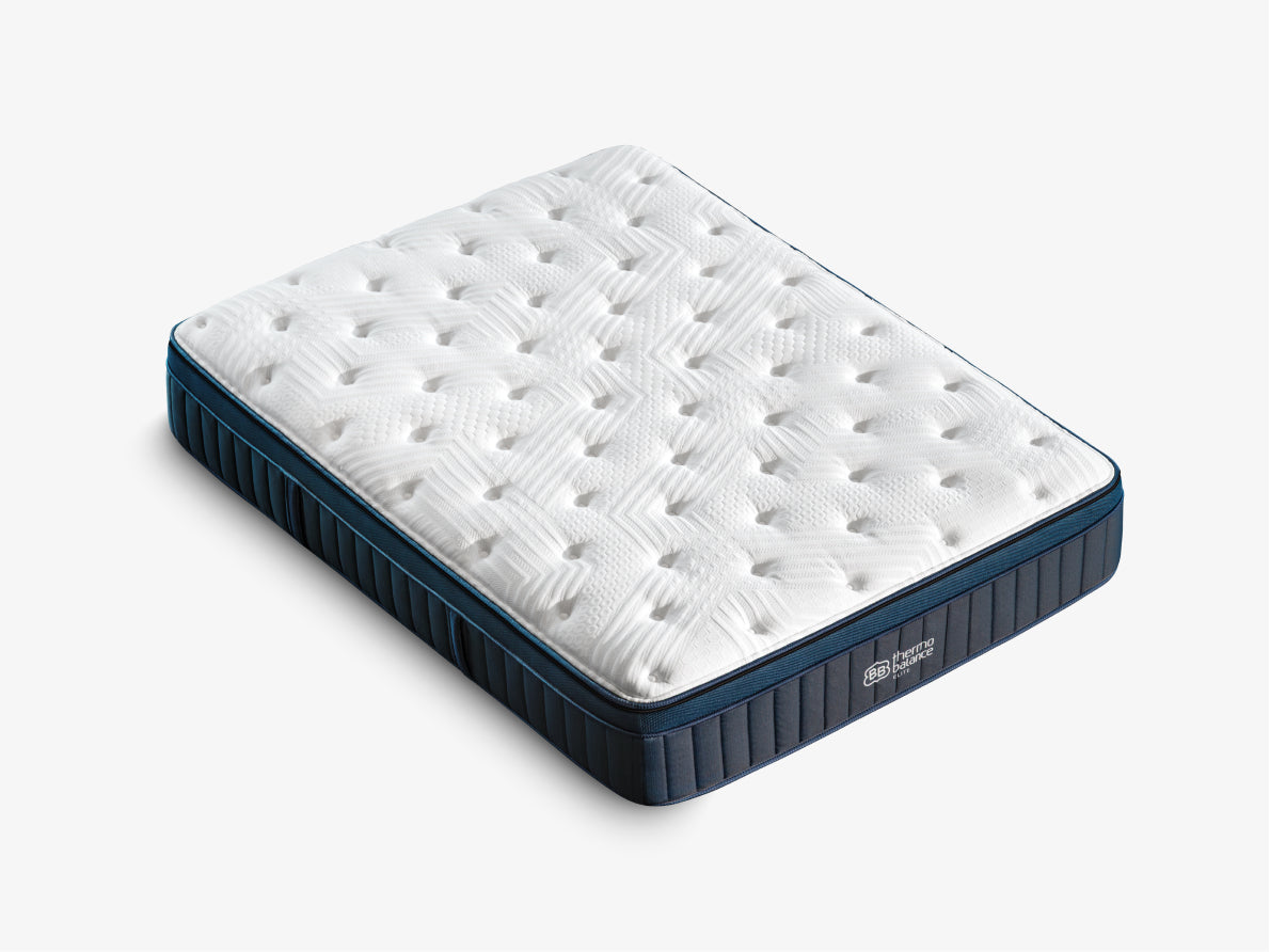 Brooklyn Bedding ThermoBalance LX Elite Mattress corner close-up showing the white quilted top and dark blue side panel on a cream bed frame.